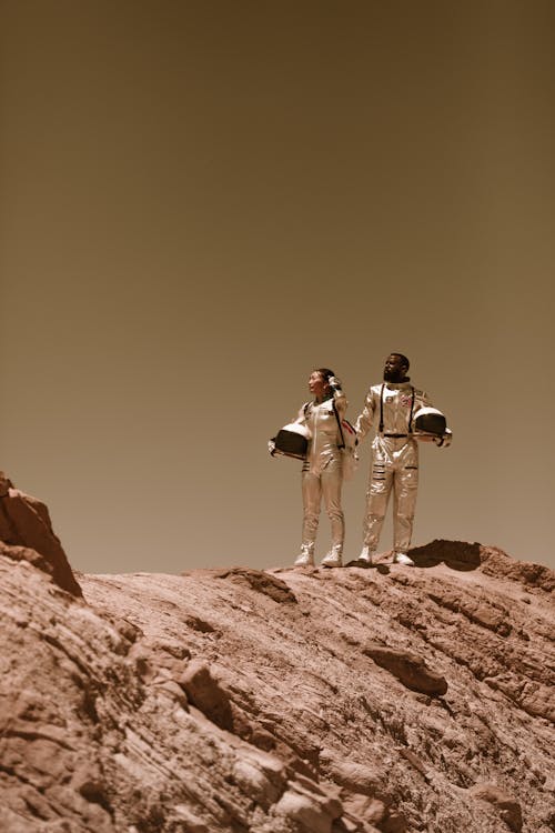 Man and Woman in Spacesuits Standing on Brown Rock Mountain