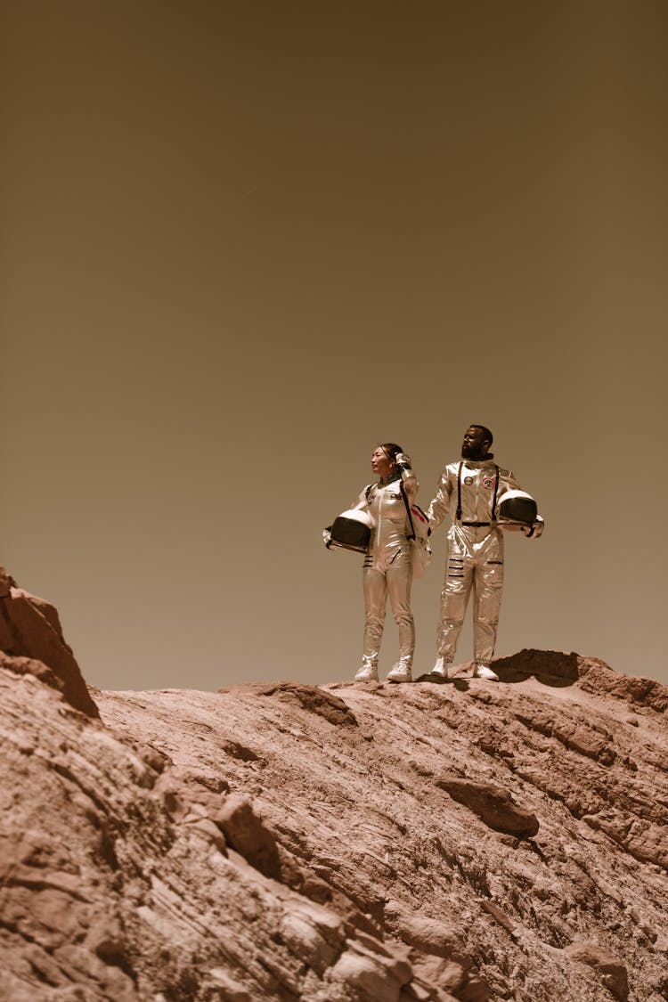 Man And Woman In Spacesuits Standing On Brown Rock Mountain