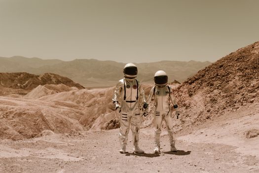 Two astronauts hold hands in a barren desert landscape, evoking a space exploration theme.