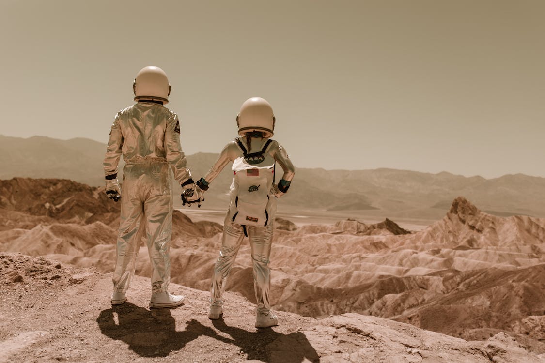 Free Astronauts Holding Hands Standing on Brown Mountains Stock Photo