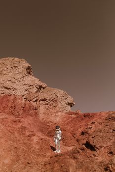 A lone astronaut in a space suit exploring rocky, Mars-like desert terrain.