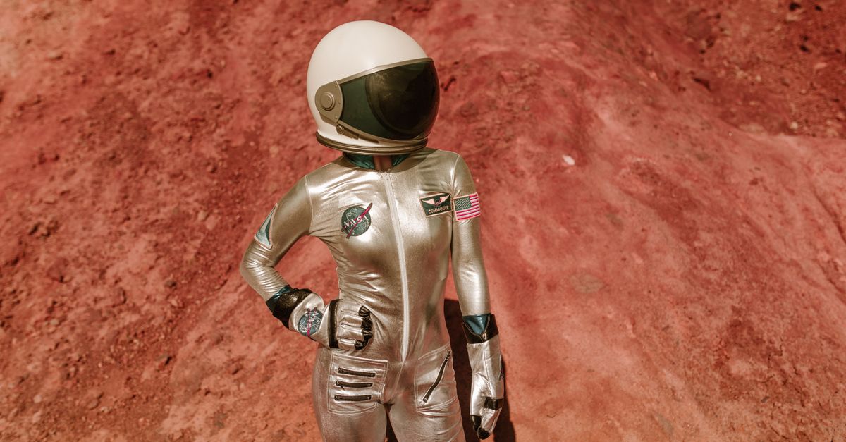 Astronaut in a white spacesuit standing on a reddish surface with a habitat dome in the background