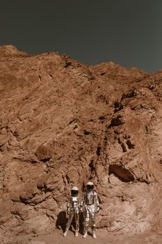 Two astronauts in suits explore a rocky, extraterrestrial landscape.