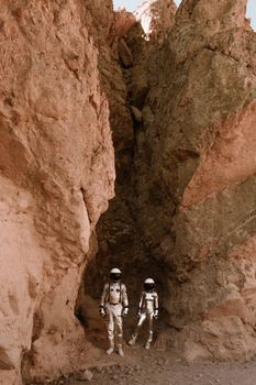 Two astronauts in suits exploring a rocky, desert-like environment resembling Mars.