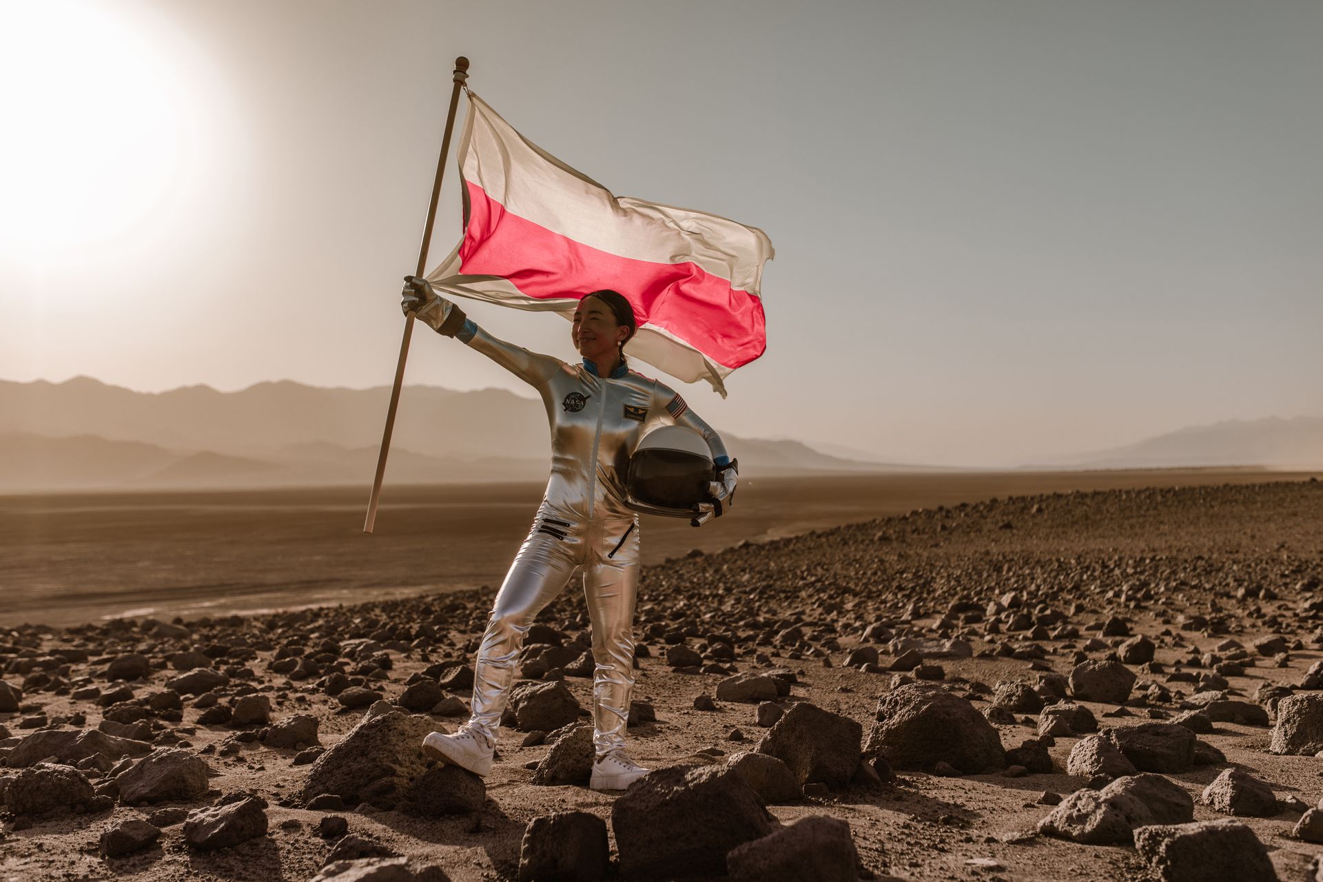 A Female Astronaut Holding the Flag of Belarus in a Barren Landscape