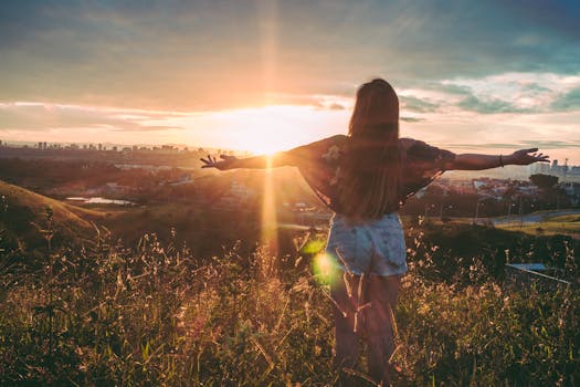 Woman Stands on Mountain over Field Under Cloudy Sky at Sunrise