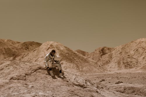 Free A Man in Space Suit Sitting on a Dry Rocky Ground Stock Photo