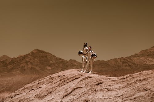 Man and Woman in Spacesuits Standing on a Barren Hill