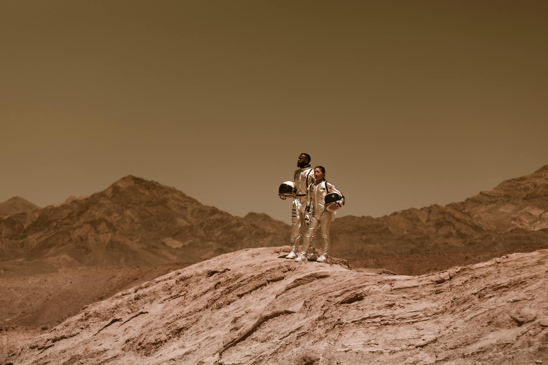 Man and Woman in Spacesuits Standing on a Barren Hill