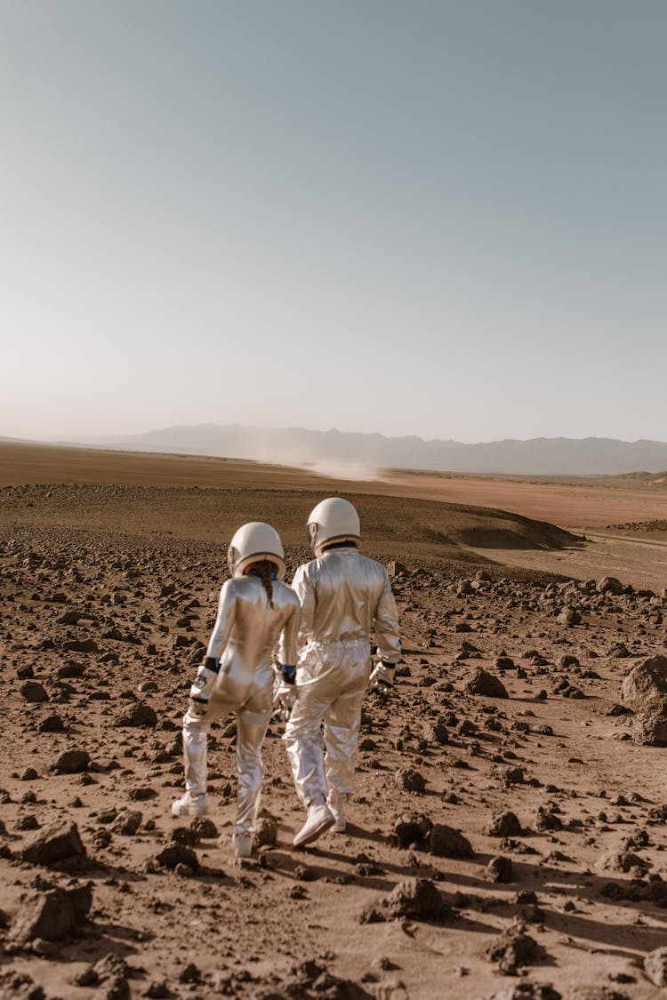 Back View Of Astronauts Holding Hands While Walking In A Desolate Planet