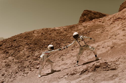 Free Astronauts Helping Each Other to Climb a Mountain Stock Photo