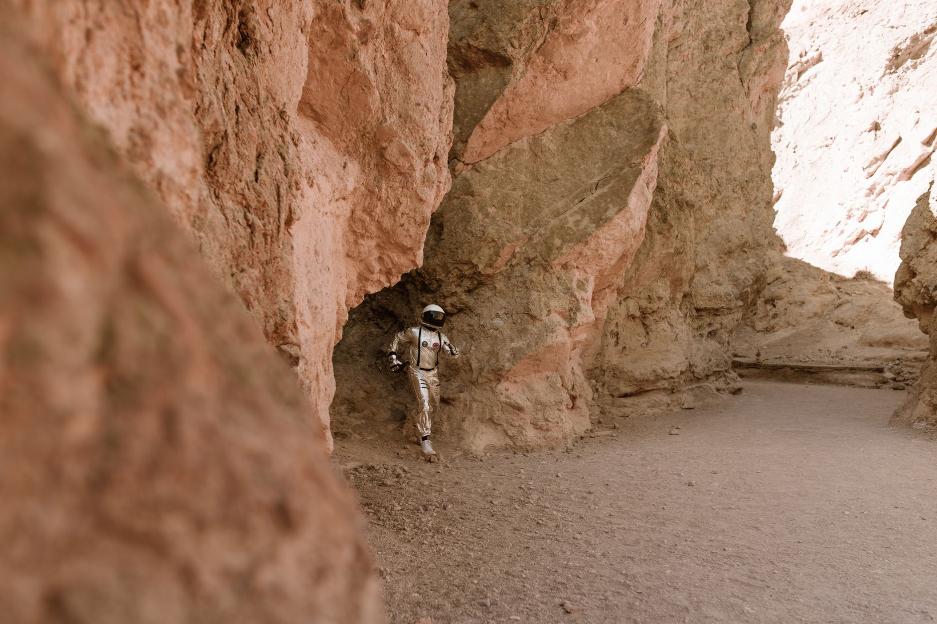 An astronaut in a suit explores a rocky canyon, resembling an alien landscape, under daylight.