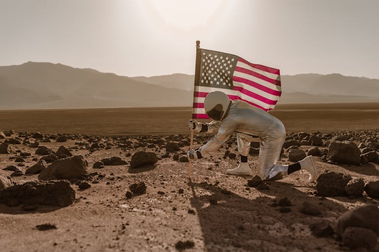 Man In Silver Spacesuit Placing An American Flag On Ground