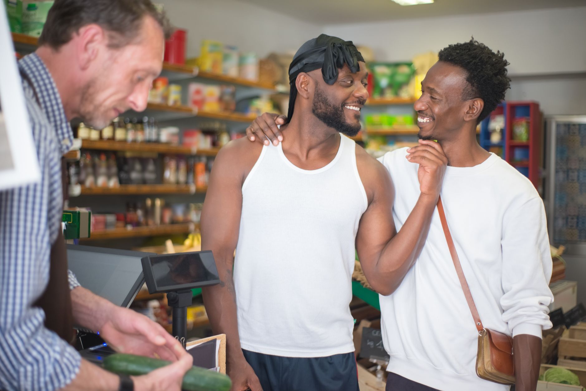 Two men share a friendly moment in a Portuguese grocery store with a clerk.