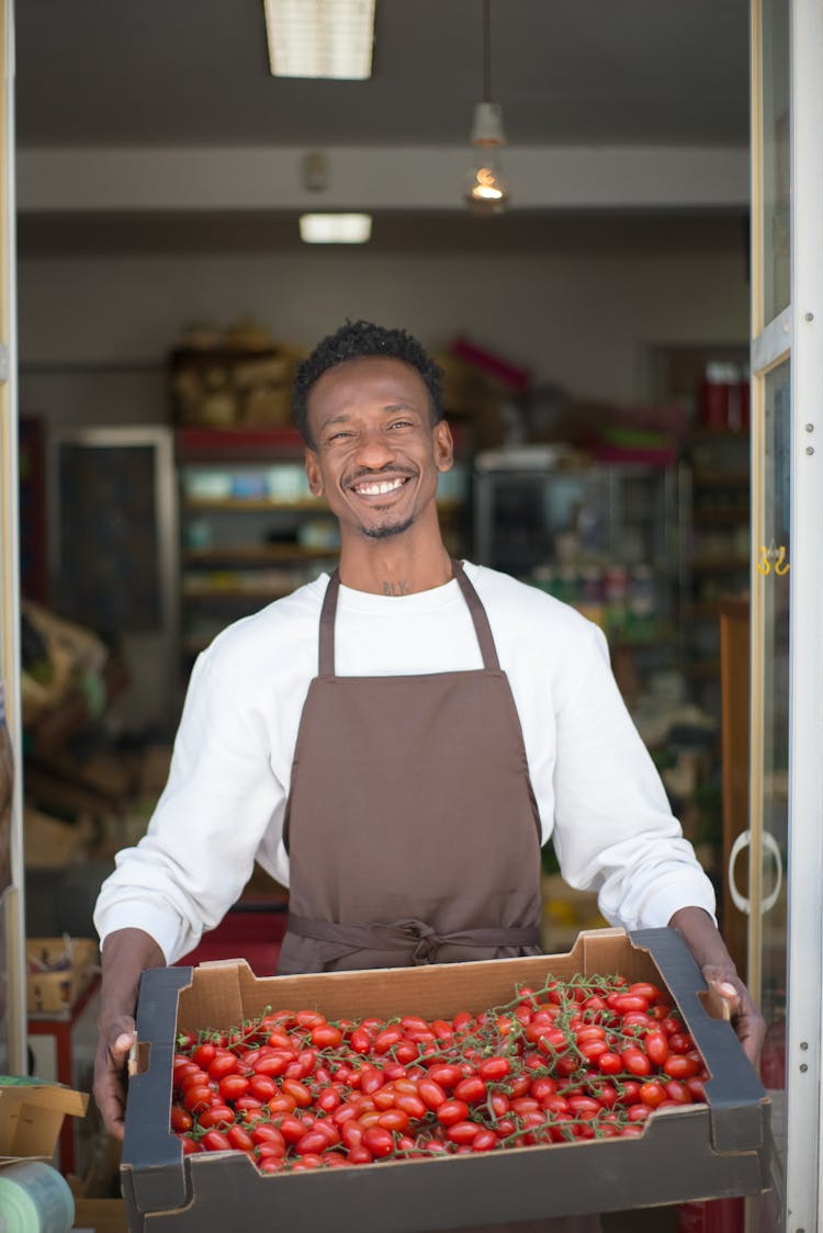 A Happy Store Clerk Holding A Crate Of Fruits