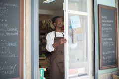 A man in an apron opens a grocery store door in Portugal, ready for business.
