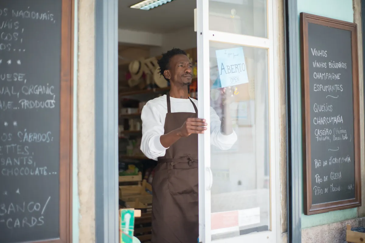 A shop owner in an apron opening their local store for the day, illustrating that each location competes in its own neighbourhood
