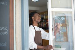 African man closing a store with a sign in Portuguese, wearing an apron.