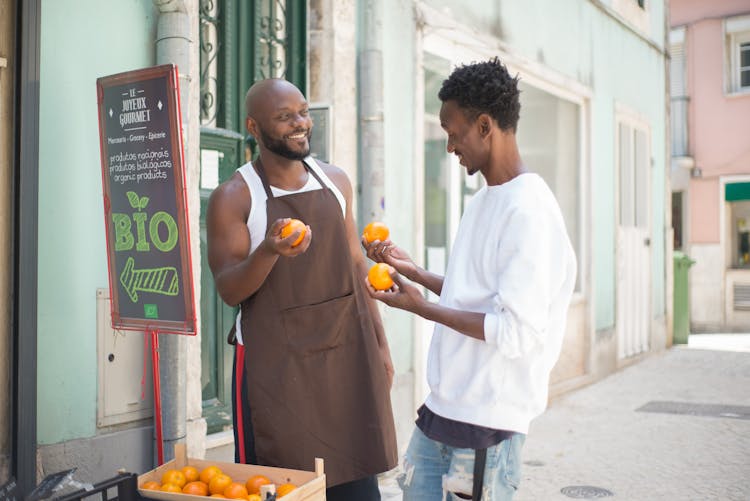 A Seller Talking To His Customer While Holding Orange Fruits