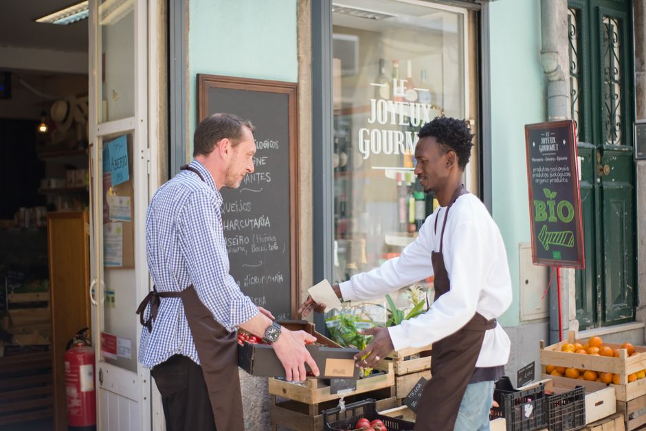 Two men arranging fruits and vegetables outside a store in Portugal.