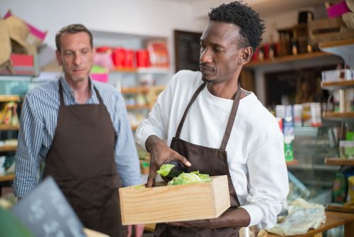 Free Men working in a grocery store arranging fresh vegetables and fruits. Indoor setting, focused on organic produce. Stock Photo