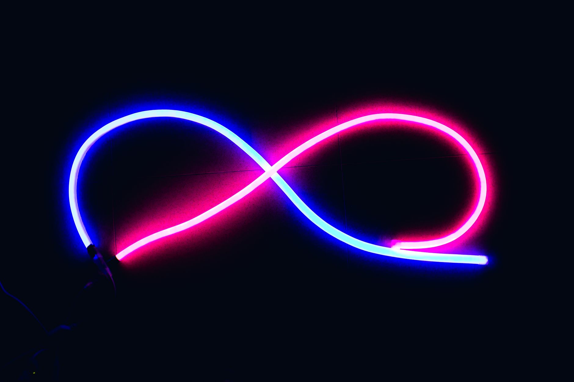 Vibrant neon infinity symbol glowing in blue and pink against a dark backdrop, evoking endless possibilities.
