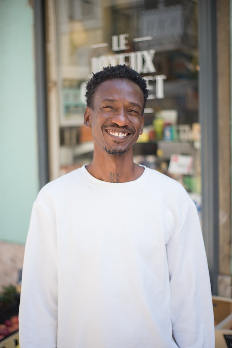 Smiling Man Wearing A White Long Sleeve Shirt Standing On Storefront