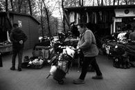 Black and white image of a woman pushing a cart among street vendor stalls in an outdoor market.