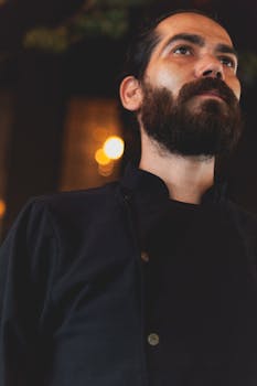 Serious male chef with beard in uniform, low angle indoor shot.