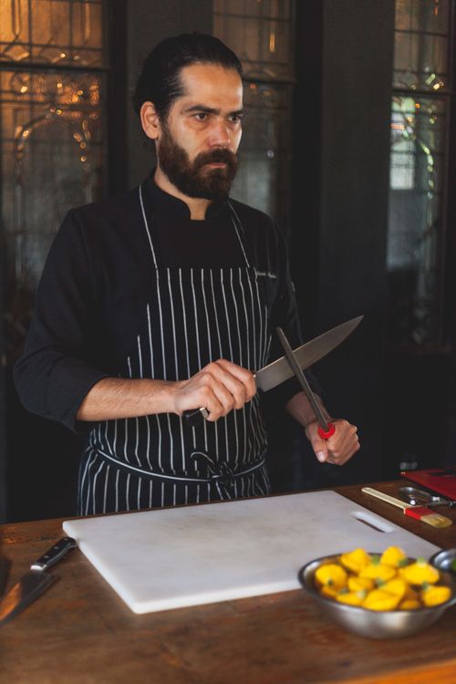 Free A skilled chef sharpening his knife in a well-lit kitchen, ready for culinary preparation. Stock Photo