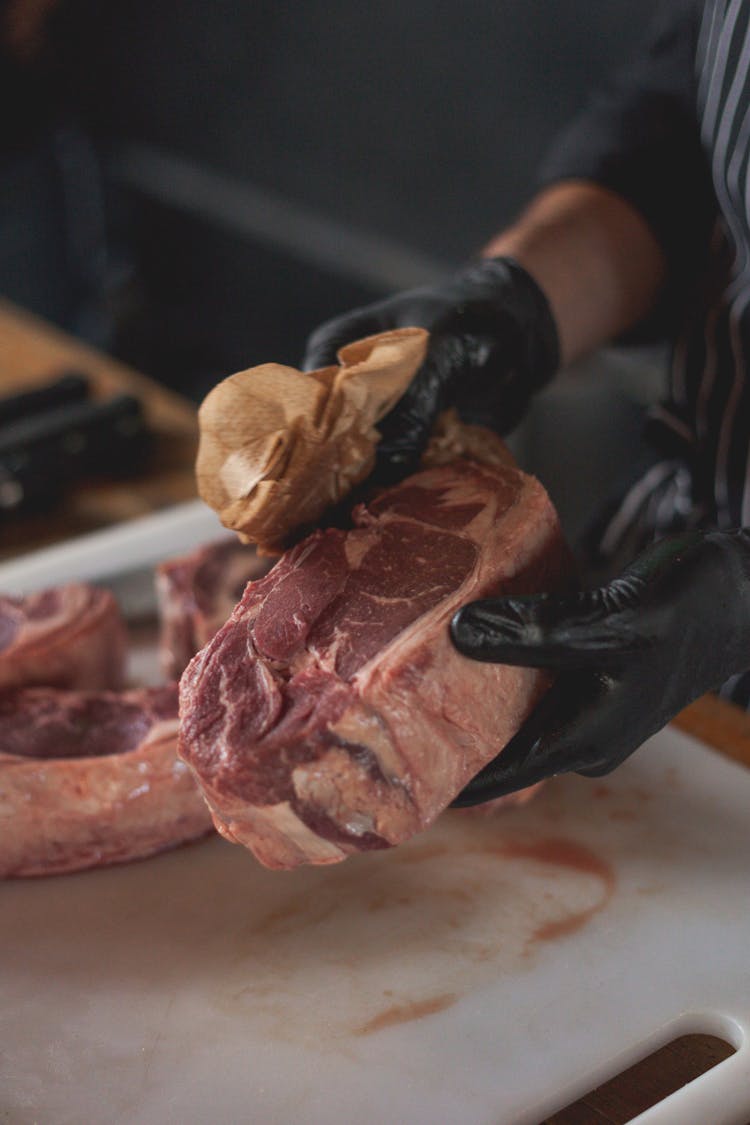 A Person Wiping Raw Steak With Paper Towel