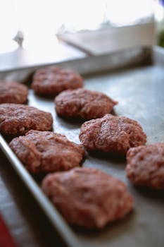Close-up of raw beef patties on a metal tray ready for cooking.