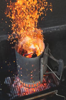 Close-up of a chimney starter with blazing charcoal and vibrant sparks.