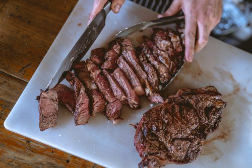 Free Top view of hands slicing a perfectly grilled steak on a chopping board, showcasing mouthwatering tenderness. Stock Photo