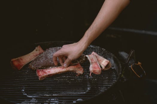 Close-up of a hand arranging bone marrow and meat on a charcoal grill for cooking.