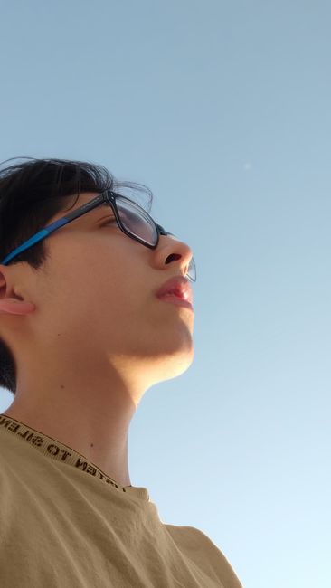 Low-angle portrait of a young man with eyeglasses gazing at a clear blue sky, captured outdoors.