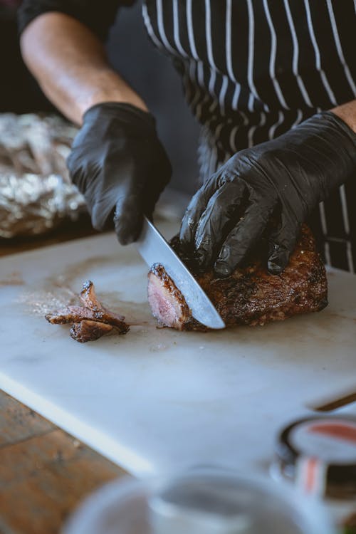 Person Slicing Meat on White Chopping Board