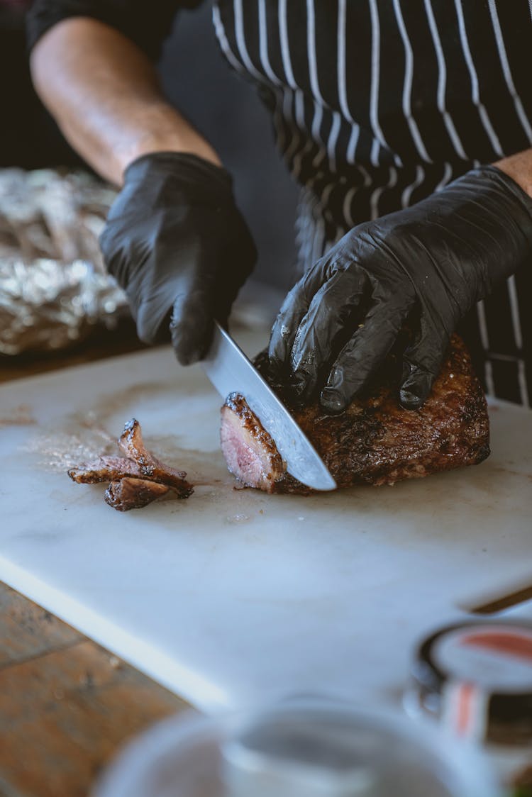 Person Slicing Meat On White Chopping Board