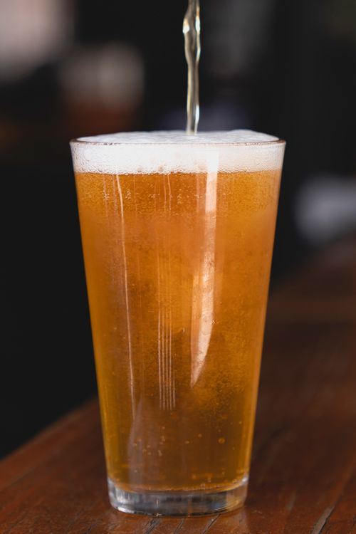 Free Close-up shot of a refreshing golden beer being poured into a glass, showcasing a foamy head. Stock Photo