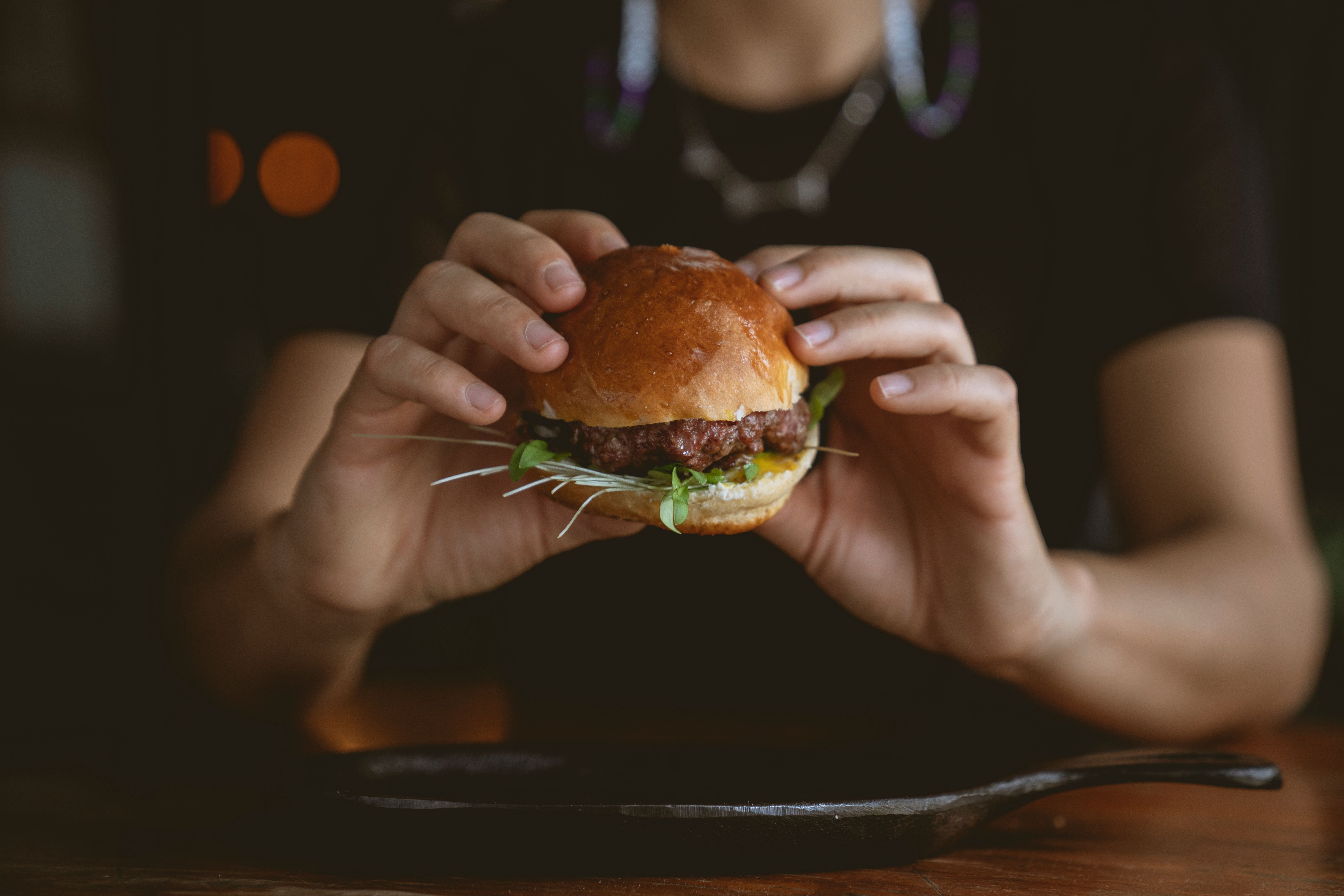 Golden-brown Moroccan spiced lamb burger on a soft brioche bun, topped with creamy harissa yogurt sauce, fresh mint leaves, and thin red onion slices