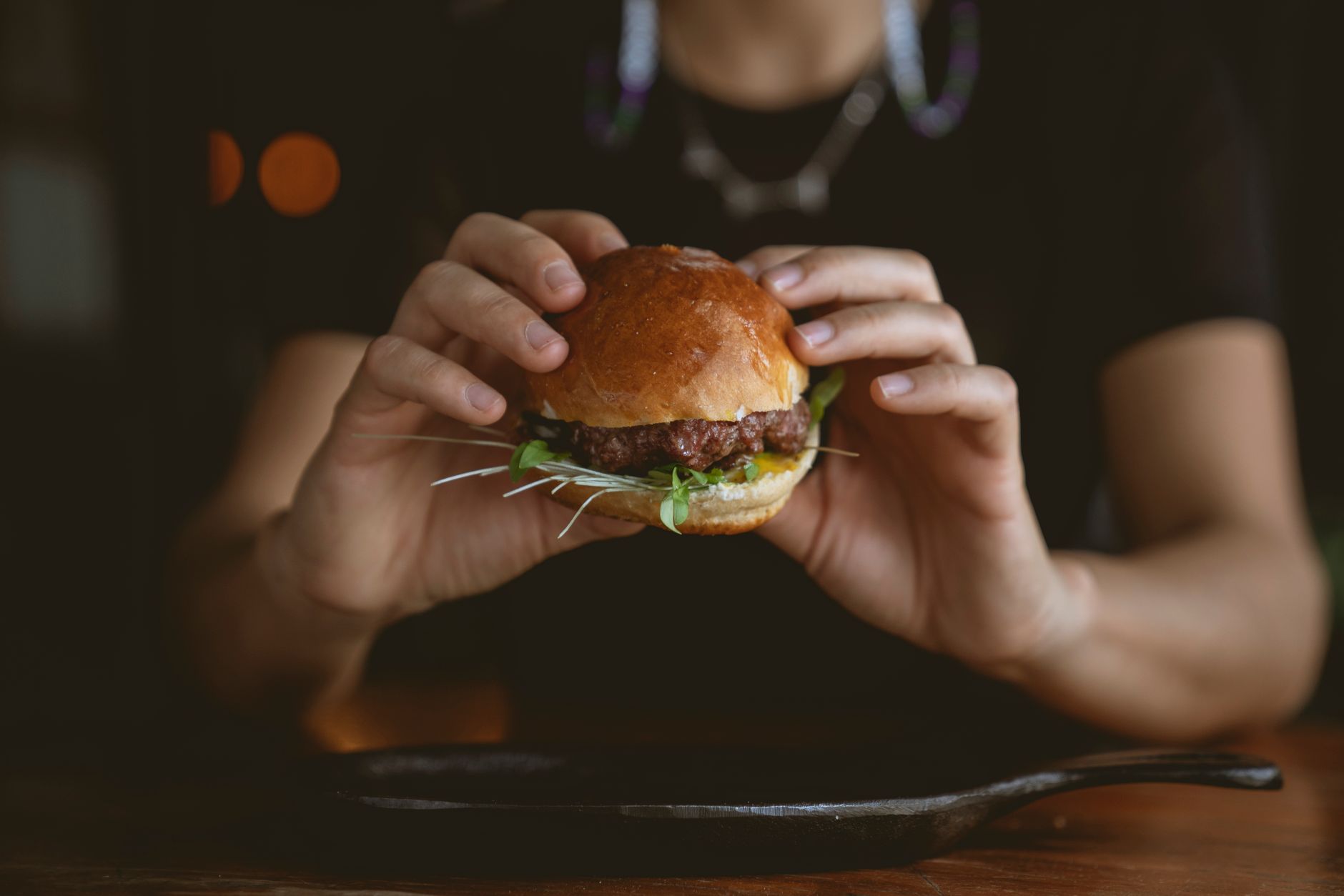 Golden-brown Moroccan spiced lamb burger on a soft brioche bun, topped with creamy harissa yogurt sauce, fresh mint leaves, and thin red onion slices