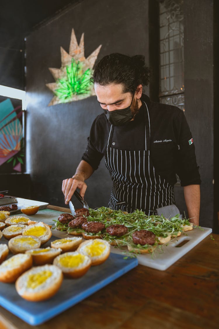 Man Wearing An Apron Preparing A Bunch Of Hamburgers