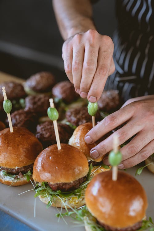 Free Chef arranging gourmet sliders with toppings on a wooden board, showcasing food preparation. Stock Photo