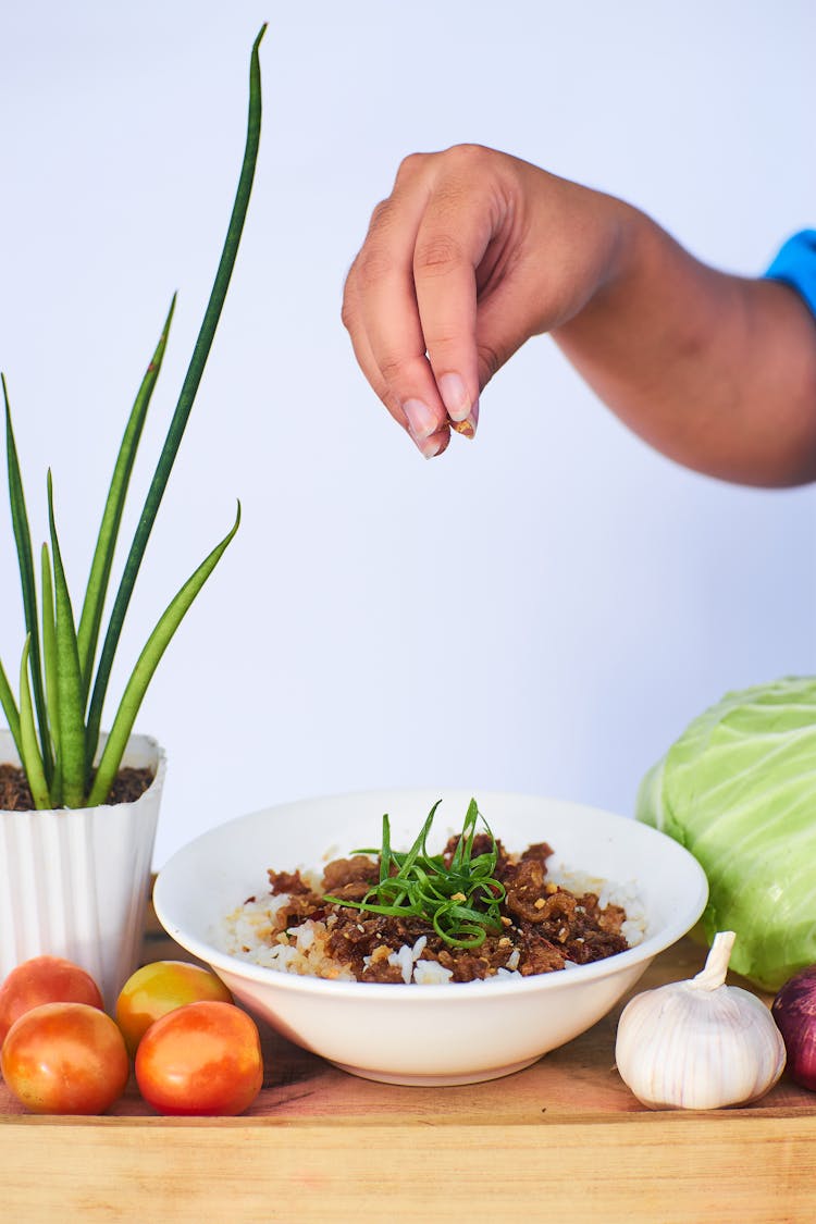 Person Putting Garnish On Cooked Food