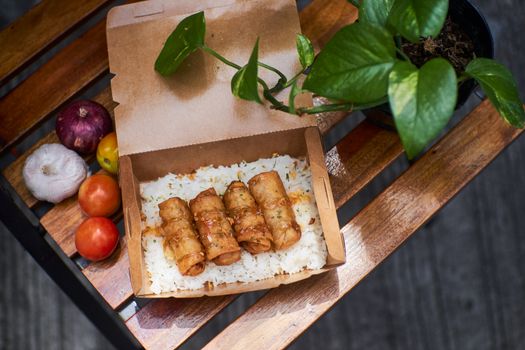 Delectable spring rolls served with rice in a recyclable box for a tasty lunch experience.