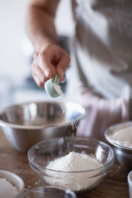 An open box of baking soda next to a small measuring spoon holding a leveled teaspoon of the white powder on a kitchen counter.