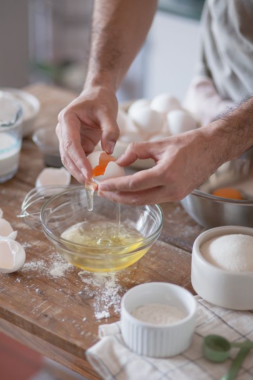 Free Hands cracking eggs into a bowl amidst flour and sugar on a wooden table. Stock Photo