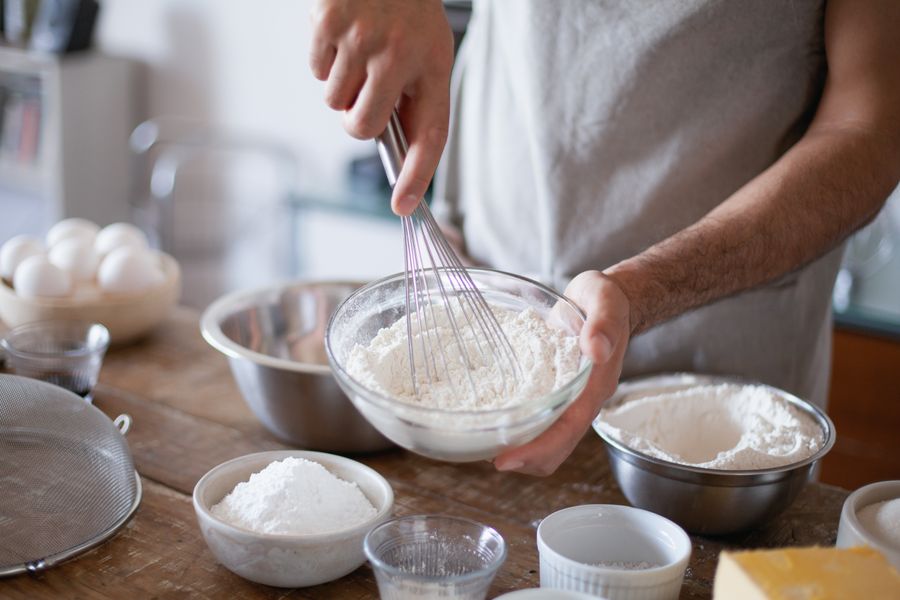 Hands whisking flour in a glass bowl on a wooden counter — photo by Los Muertos Crew on Pexels