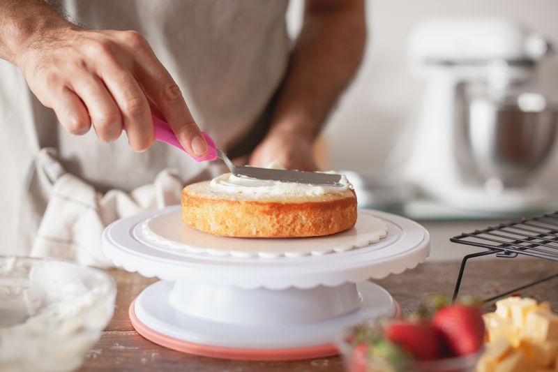 Baker carefully piping buttercream onto a layered custom cake