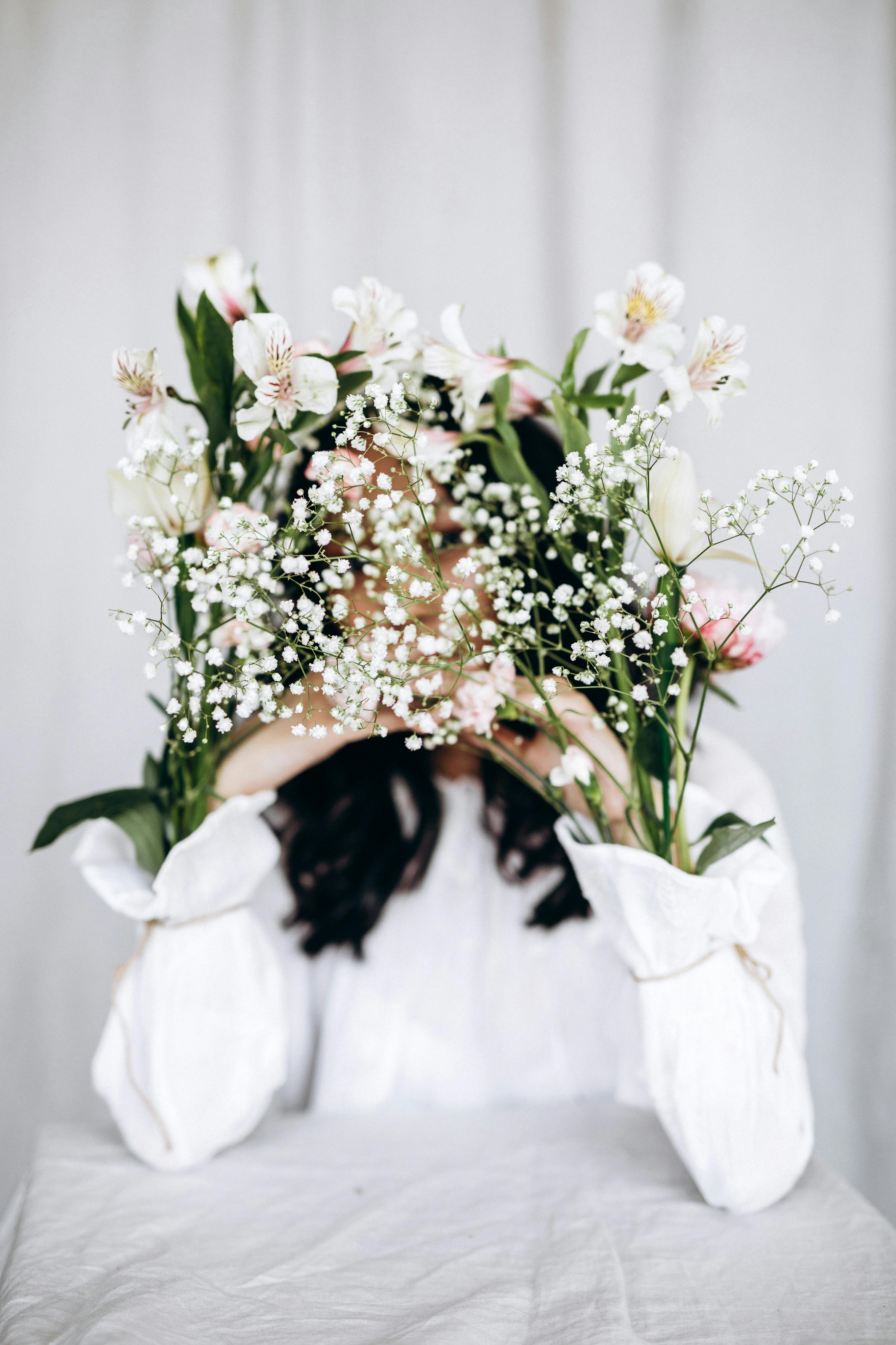 Woman holding a bouquet of white flowers in a studio with soft focus background.